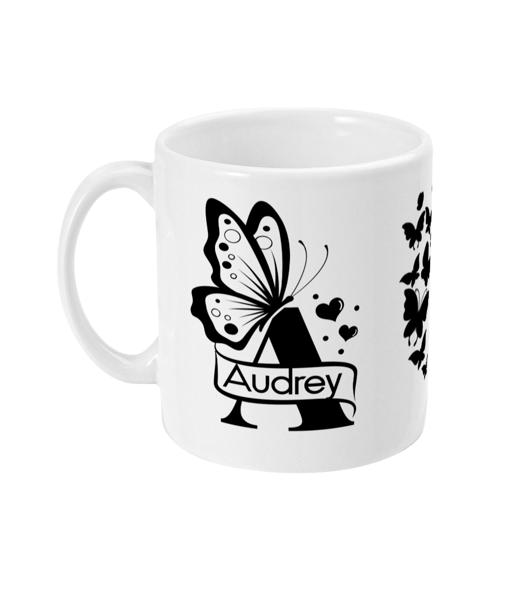 Personalised white ceramic mug with letter A monogram surrounded by butterflies and hearts, featuring the name 'Audrey' in a decorative banner.