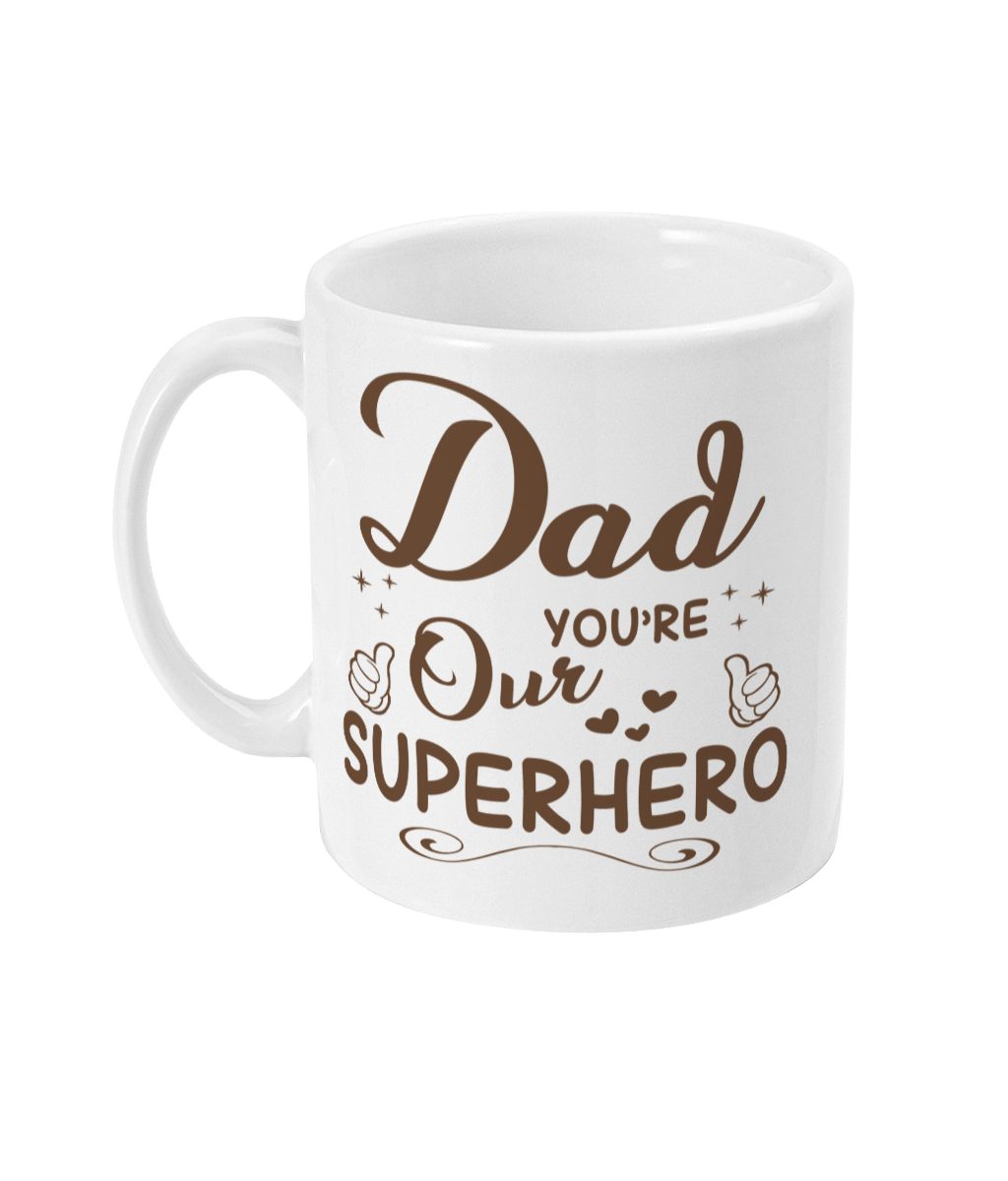White mug with brown 'Dad You're Our Superhero' text, stars, heart, and thumbs-up icons.