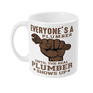 White ceramic mug with a graphic of a clenched fist holding a pipe wrench and text 'EVERYONE'S A PLUMBER UNTIL THE REAL PLUMBER SHOWS UP'.