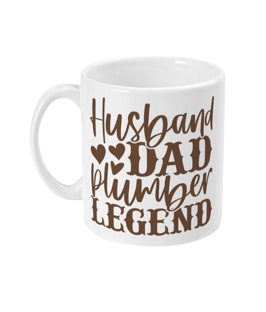 White ceramic mug with brown text that says 'Husband Dad Plumber Legend' intertwined with graphic hearts.