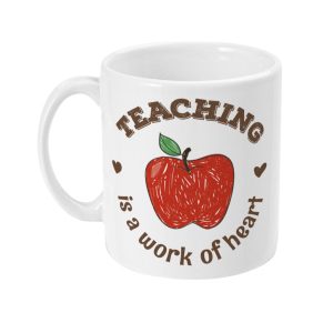 White mug with large red apple, green leaf, and text 'TEACHING is a work of heart' surrounded by small heart shapes.