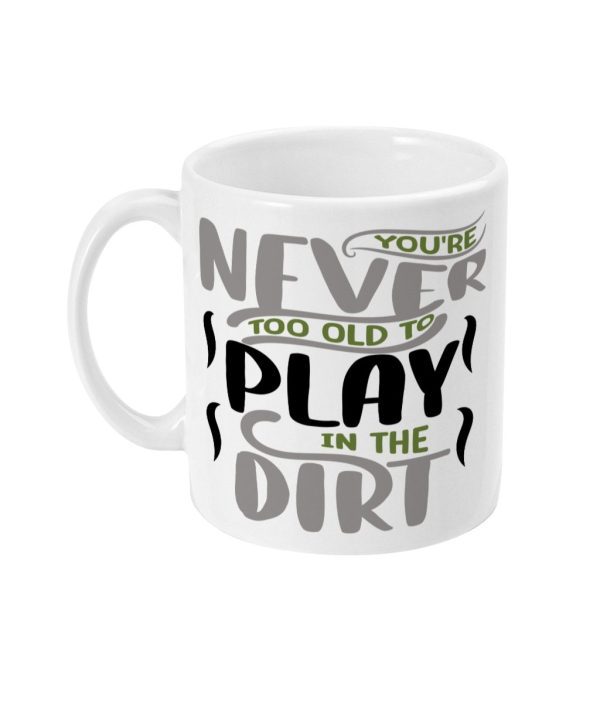 White ceramic mug with text design: 'YOU'RE NEVER TOO OLD TO PLAY IN THE DIRT' in black, green, and gray fonts.